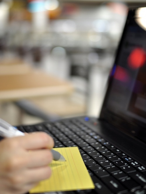 someone writing a note while looking at a laptop